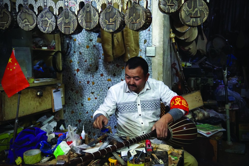 An instrument maker named Muhammad puts the finishing touches on a tembur in his workshop. Muhammad also wears a red badge on his sleeve, signifying he is part of the “community watch”, a form of self-policing initiated by the central government.