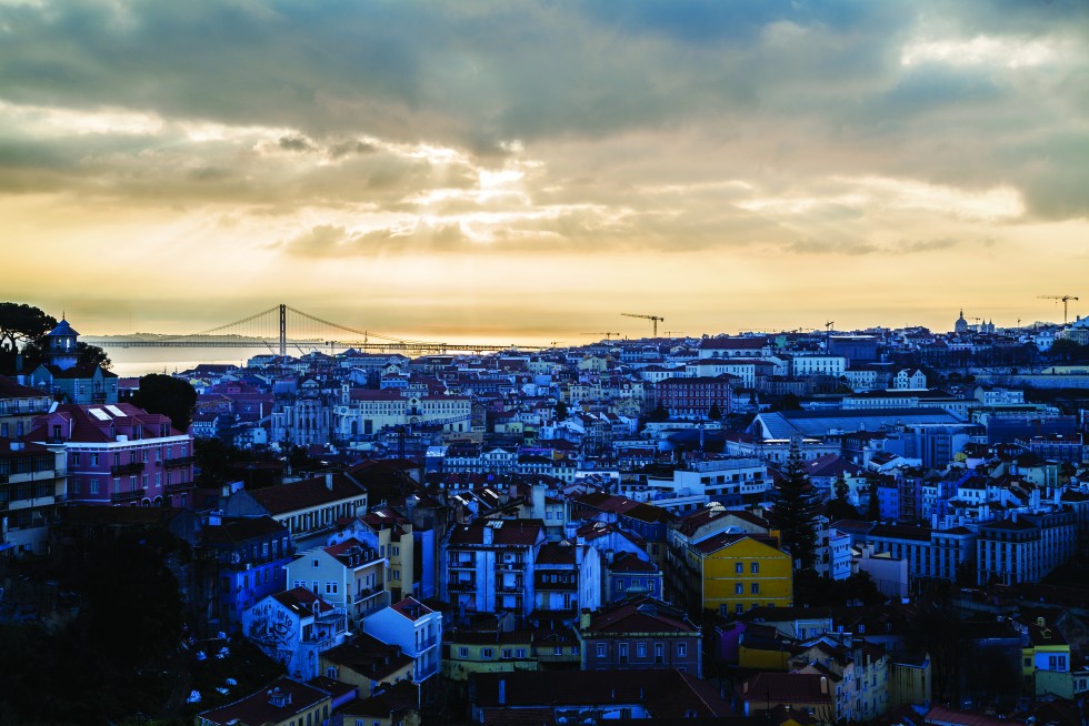 Lisbon, Portugal: Dust-drenched shafts dwell on cracked seams, the forest-spires of aerials and satellite bowls, air conditioners’ square heads prophesying long bronze colonnades and blue tile façades receding into fire escapes, distant cranes of half-built halls, the sky’s mauve tufts shadowed by d