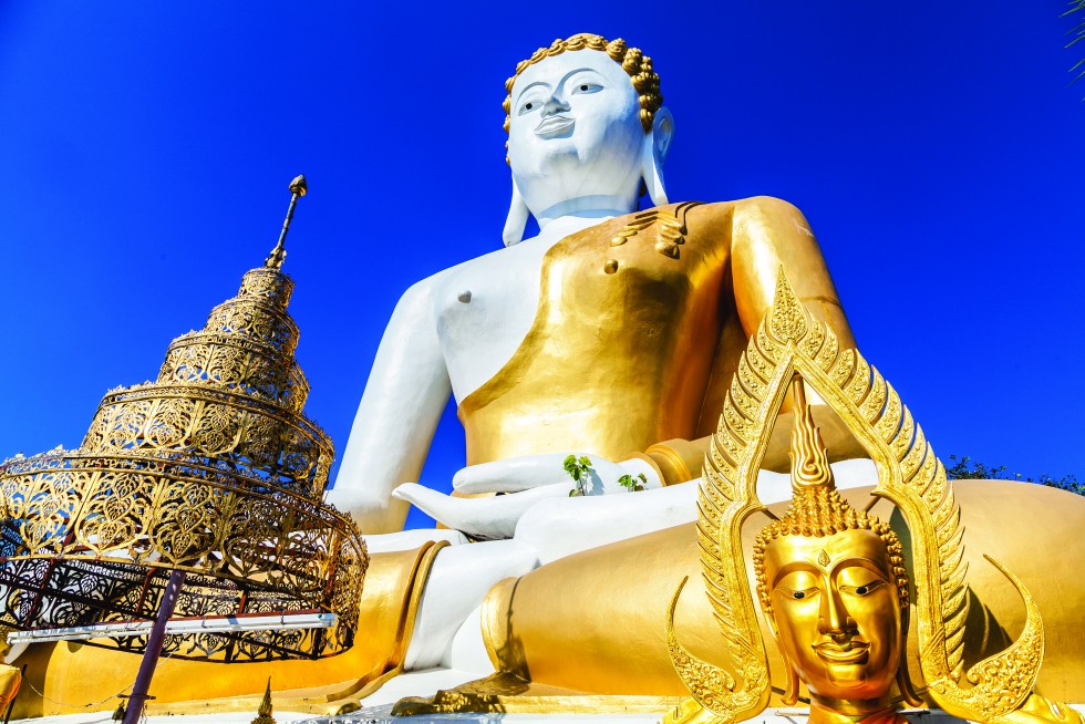 Huge seated Buddha figure on a hill at Wat Phra That Doi Kham, or Golden Temple. Hill tribe girls gather on the stairs in traditional outfits for photo opportunities.