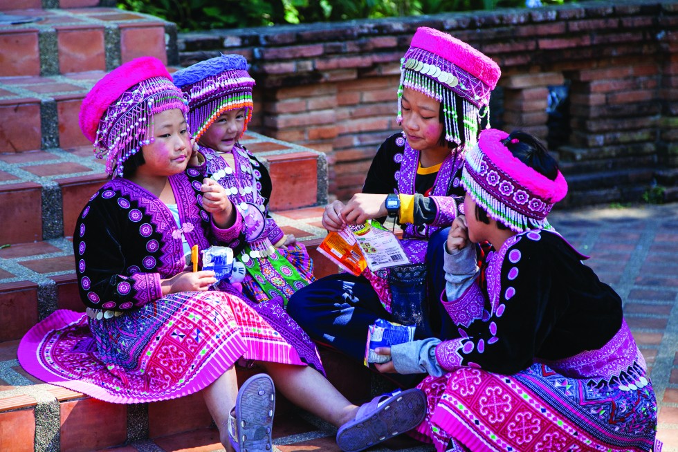 Huge seated Buddha figure on a hill at Wat Phra That Doi Kham, or Golden Temple. Hill tribe girls gather on the stairs in traditional outfits for photo opportunities.