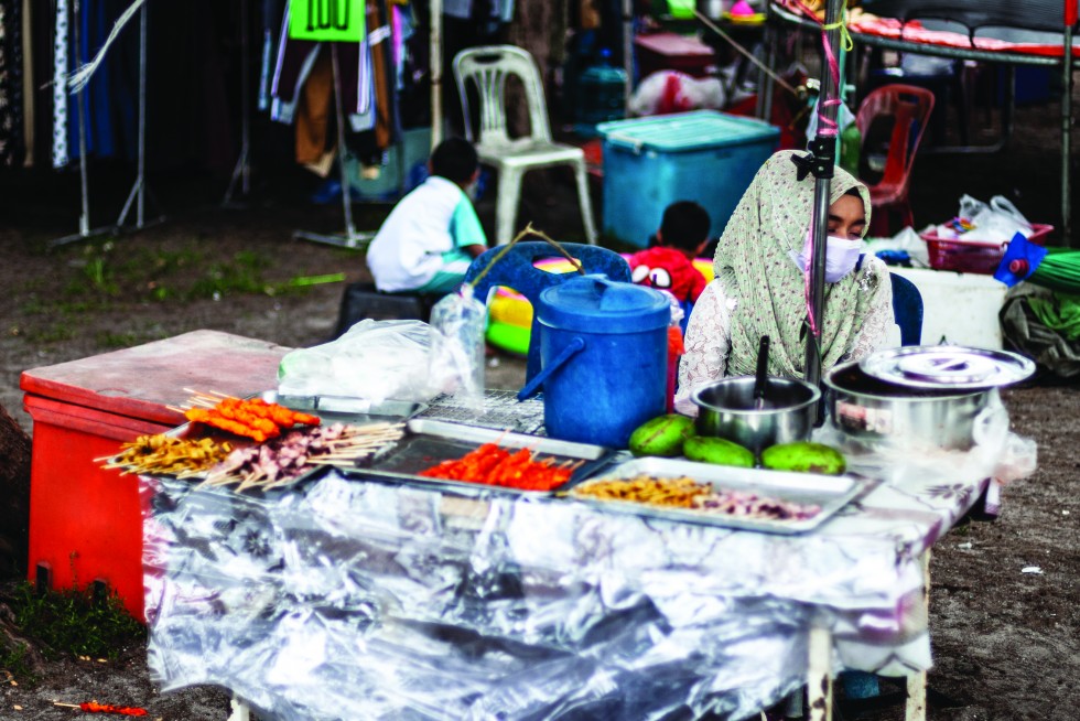 At a carnival along the shore a vendor takes a nap and a girl goes shopping.